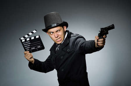 Young man with weapon and clapboard against grayの写真素材