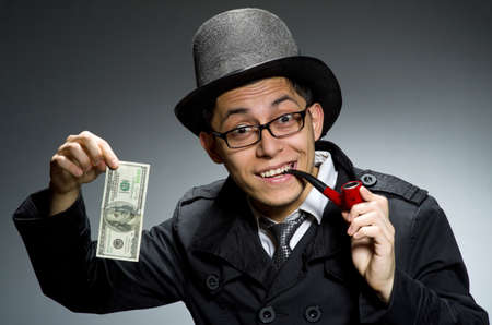 Young detective in black coat with money against gray