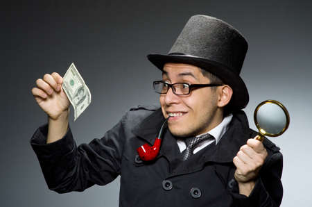Young detective in black coat with money against gray