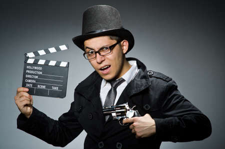 Young man with weapon and clapboard against grayの写真素材