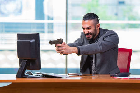 Angry aggressive businessman with gun in the officeの写真素材