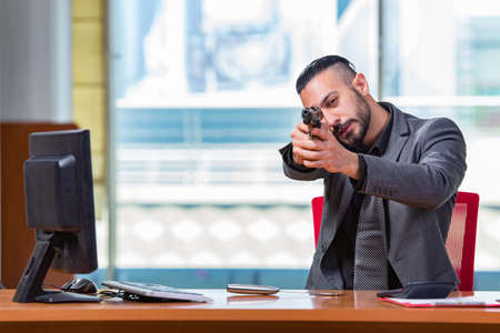 Angry aggressive businessman with gun in the officeの写真素材