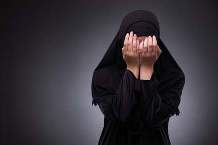 Muslim woman in black dress against dark background
