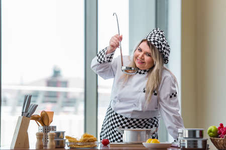 Female cook preparing soup in brightly lit kitchenの写真素材