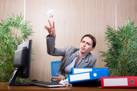 Woman under stress tossing papers in the officeの写真素材