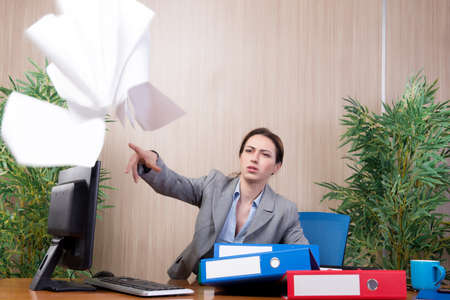 Woman under stress tossing papers in the officeの写真素材