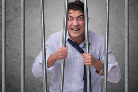 Young businessman behind the bars in prisonの写真素材