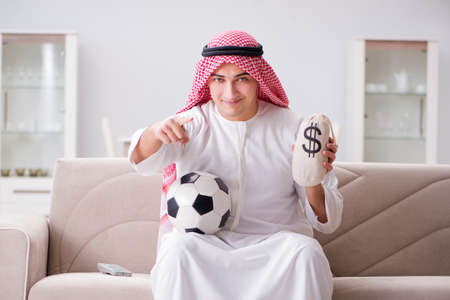 Young arab man watching football sitting on sofaの写真素材
