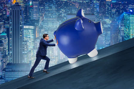 Man pushing piggybank uphill in business conceptの写真素材