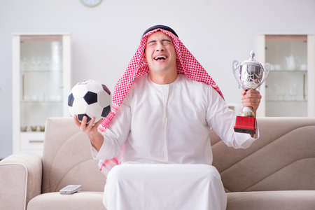 Young arab man watching football sitting on sofaの写真素材