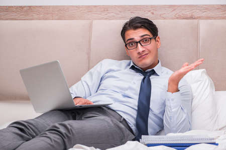 Businessman working in the bed at homeの写真素材