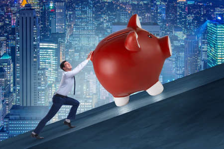 Man pushing piggybank uphill in business conceptの写真素材