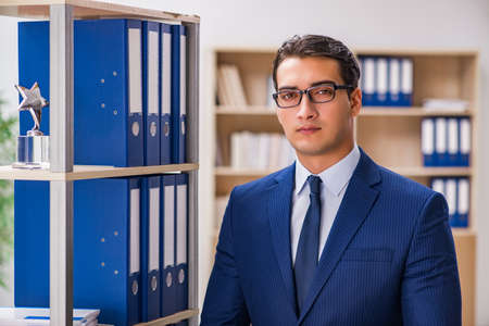 Young man standing next to the shelf with folders