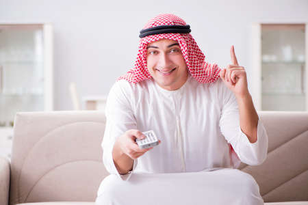Young arab man watching tv sitting on the sofaの写真素材