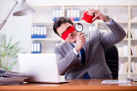 Blindfold businessman sitting at desk in officeの写真素材