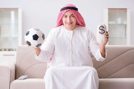 Young arab man watching football sitting on sofaの写真素材
