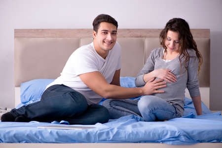 Young family with pregnant wife expecting baby in bedの写真素材