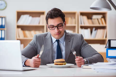 Hungry funny businessman eating junk food sandwichの写真素材