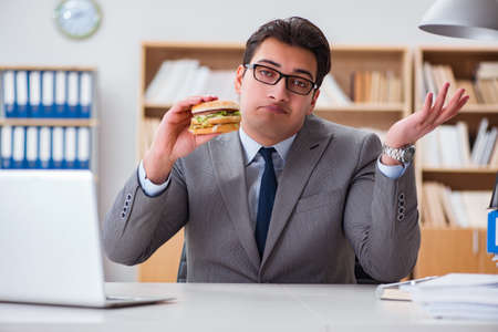 Hungry funny businessman eating junk food sandwichの写真素材
