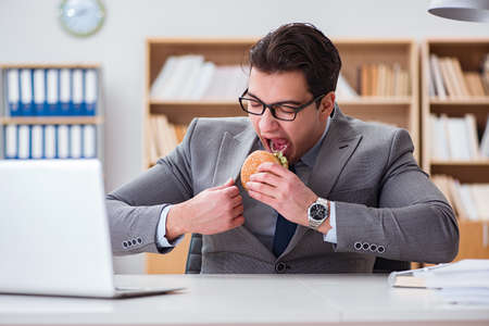 Hungry funny businessman eating junk food sandwichの写真素材