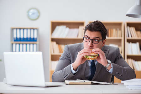 Hungry funny businessman eating junk food sandwichの写真素材