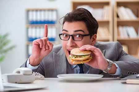 Hungry funny businessman eating junk food sandwichの写真素材