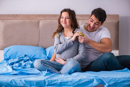 Young family with pregnant wife expecting baby in bedの写真素材