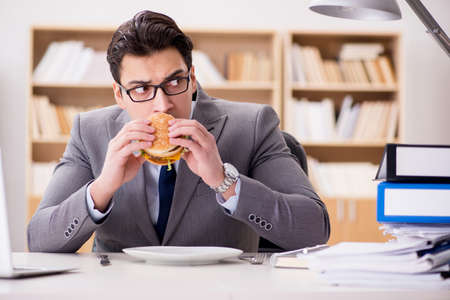 Hungry funny businessman eating junk food sandwichの写真素材