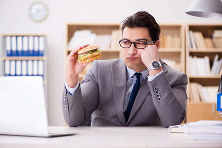 Hungry funny businessman eating junk food sandwichの写真素材