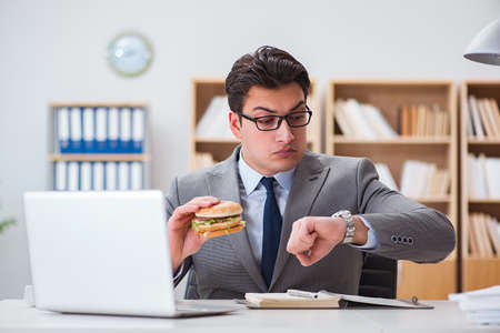 Hungry funny businessman eating junk food sandwichの写真素材