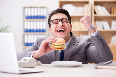 Hungry funny businessman eating junk food sandwichの写真素材