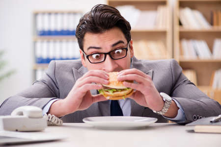 Hungry funny businessman eating junk food sandwichの写真素材