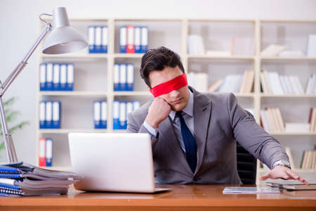 Blindfold businessman sitting at desk in officeの写真素材