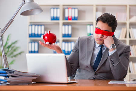 Blindfold businessman sitting at desk in officeの写真素材
