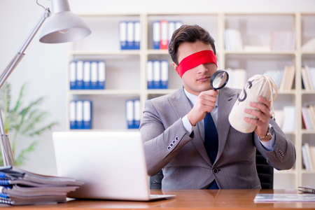 Blindfold businessman sitting at desk in officeの写真素材