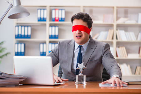 Blindfold businessman sitting at desk in officeの写真素材