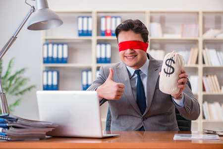 Blindfold businessman sitting at desk in officeの写真素材