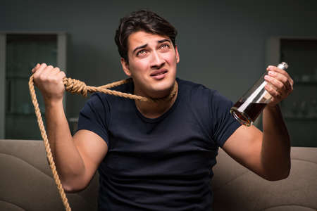Depressed man with noose around his neck while drinking alcoholの写真素材