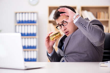 Hungry funny businessman eating junk food sandwichの写真素材