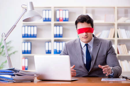Blindfold businessman sitting at desk in officeの写真素材