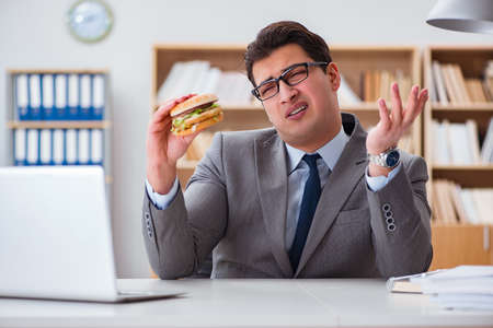 Hungry funny businessman eating junk food sandwichの写真素材
