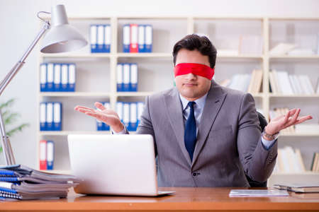 Blindfold businessman sitting at desk in officeの写真素材