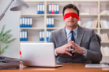 Blindfold businessman sitting at desk in officeの写真素材