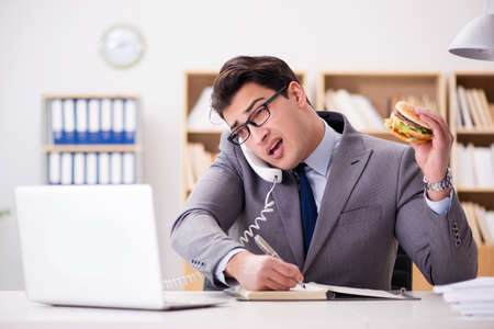 Hungry funny businessman eating junk food sandwichの写真素材