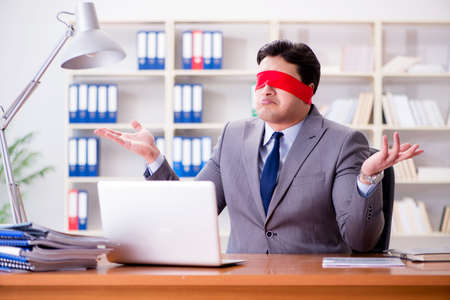 Blindfold businessman sitting at desk in officeの写真素材