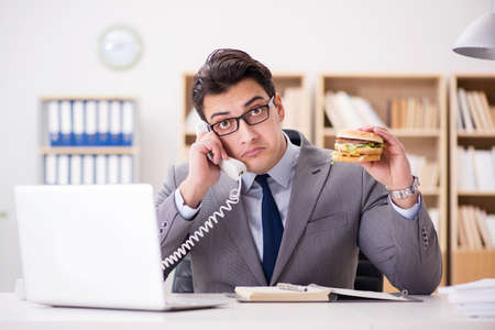 Hungry funny businessman eating junk food sandwichの写真素材