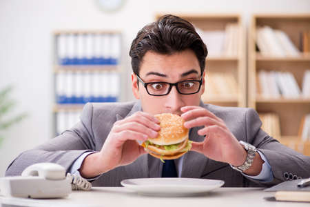 Hungry funny businessman eating junk food sandwichの写真素材