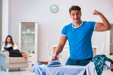 Man husband ironing at home helping his wifeの写真素材
