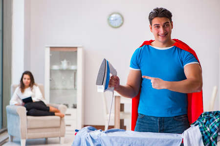 Super hero man husband ironing at home helping his wifeの写真素材