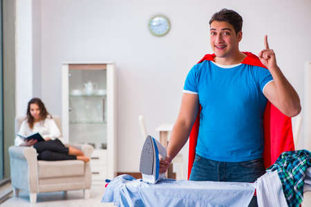 Super hero man husband ironing at home helping his wifeの写真素材